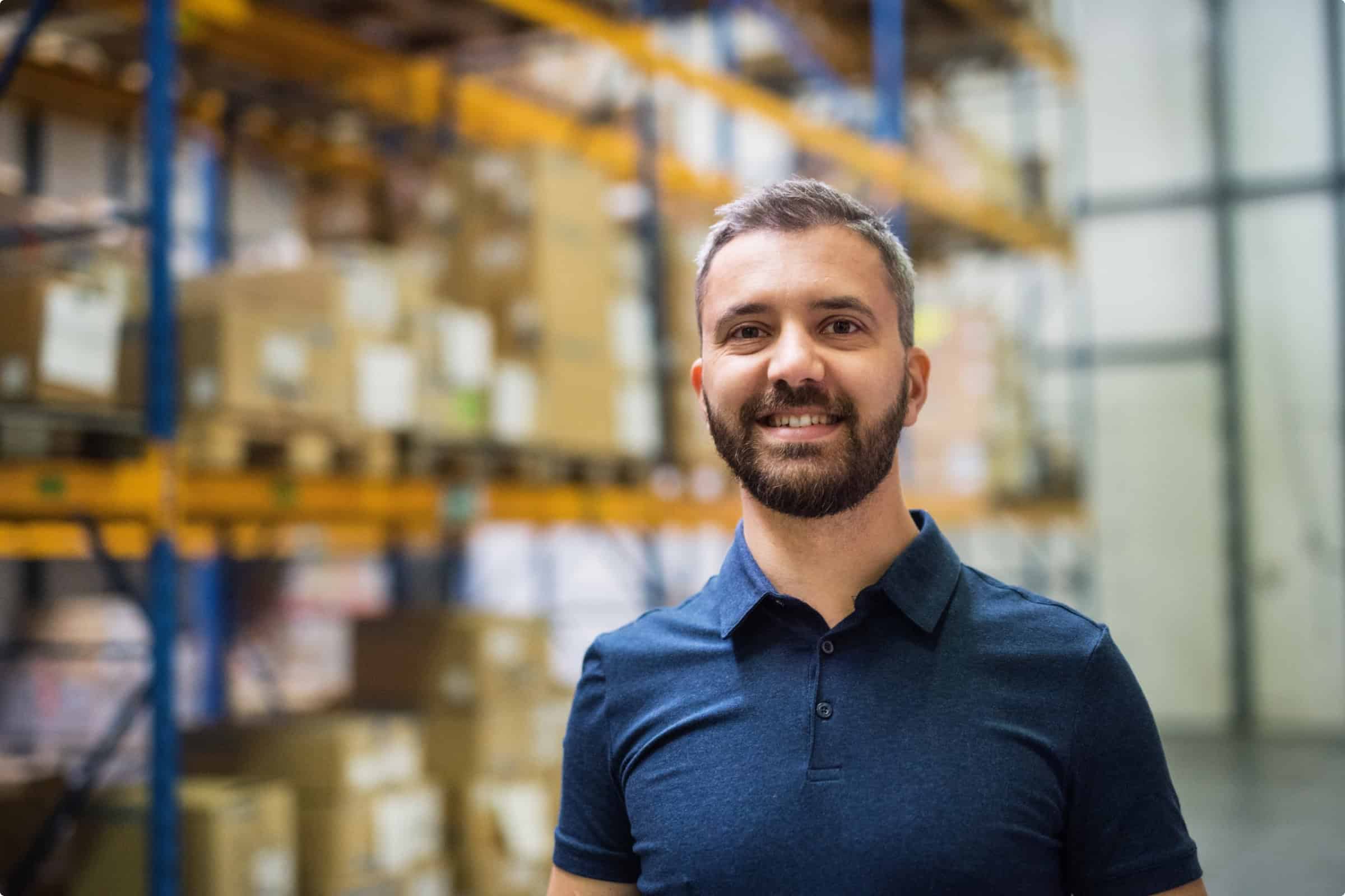 Warehouse worker smiling in a storage facility with shelves of boxes.