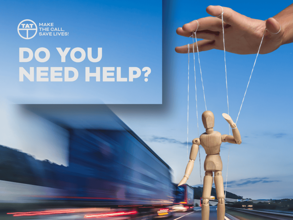 Hand controlling a wooden puppet near a moving truck with text asking “Do you need help” in a road safety campaign.