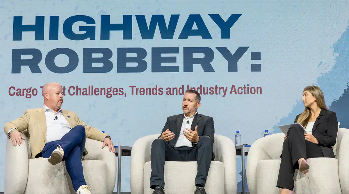 Three panelists seated on stage discussing cargo theft trends under a “Highway Robbery: Cargo Theft Challenges” session screen.